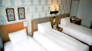 A hotel room with two single beds, a nightstand with a phone, and a wall-mounted lamp.