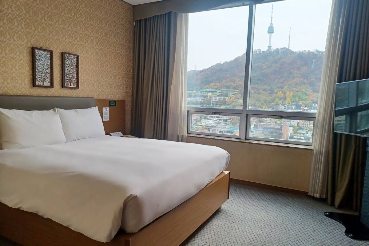 A hotel room with a large bed, a view of a cityscape, and a TV on the right side.