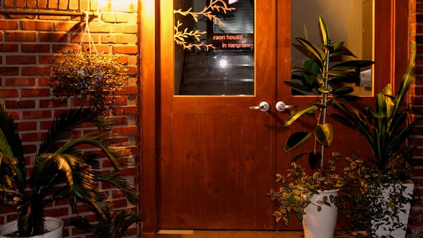 Une porte en bois avec un panneau de verre sur lequel est inscrit un texte, et de part et d’autre, des plantes en pot.