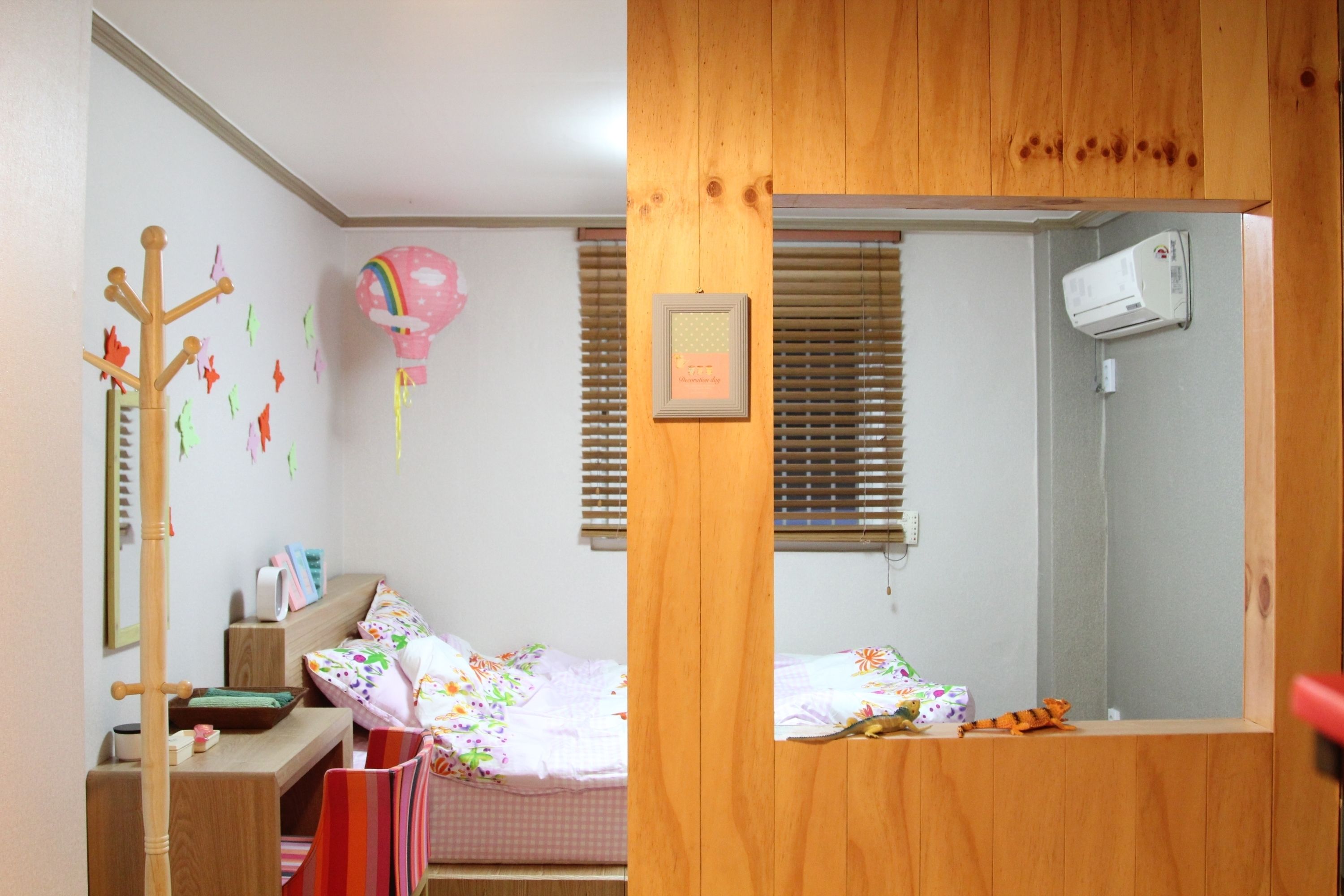 A child's bedroom with a bunk bed, a desk, a chair, a coat rack, a wall decoration, and a window with blinds.