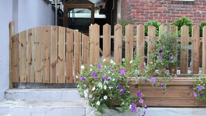 Une porte en bois et un parterre de fleurs aux couleurs violettes devant un bâtiment en briques.
