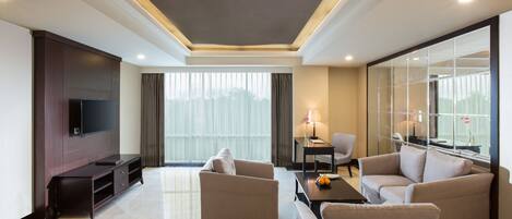 A modern hotel room with a flat-screen TV, two sofas, a coffee table, and a large window with curtains.