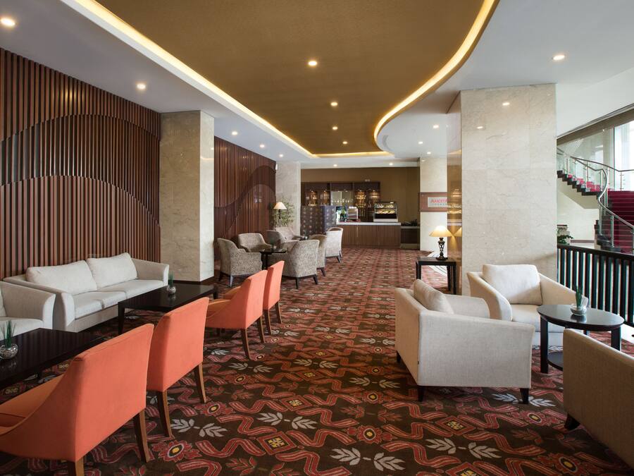 A hotel lobby with a reception desk, seating area with sofas and chairs, patterned carpet, and a staircase.