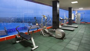 Een sportschool met diverse fitnessapparaten, grote ramen en een stadszicht.