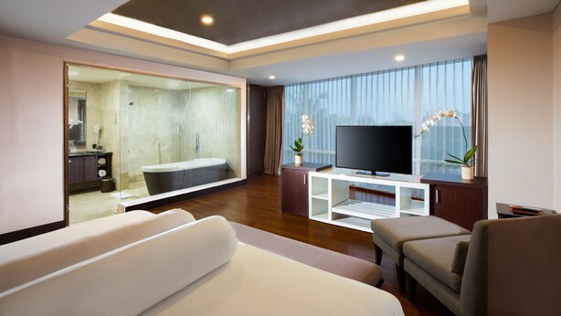 Een moderne woonkamer met een grote flatscreen televisie, een bank, een salontafel en een badkamer met glazen wanden.