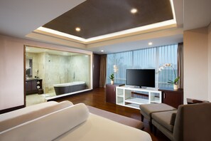 Una sala de estar moderna con un televisor de pantalla plana grande, un sofá, una mesa de centro y un baño con paredes de vidrio.
