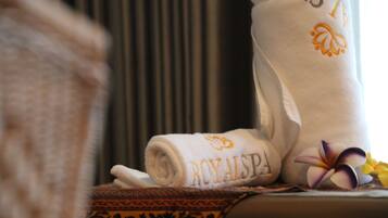 A rolled towel with "ROYALSPA" embroidered in gold, a decorative pillow, and a flower on a bed.