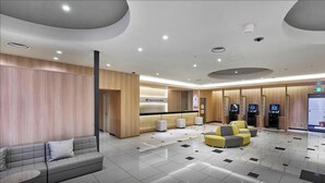 A modern hotel lobby with a reception desk, seating area, and self-service kiosks.