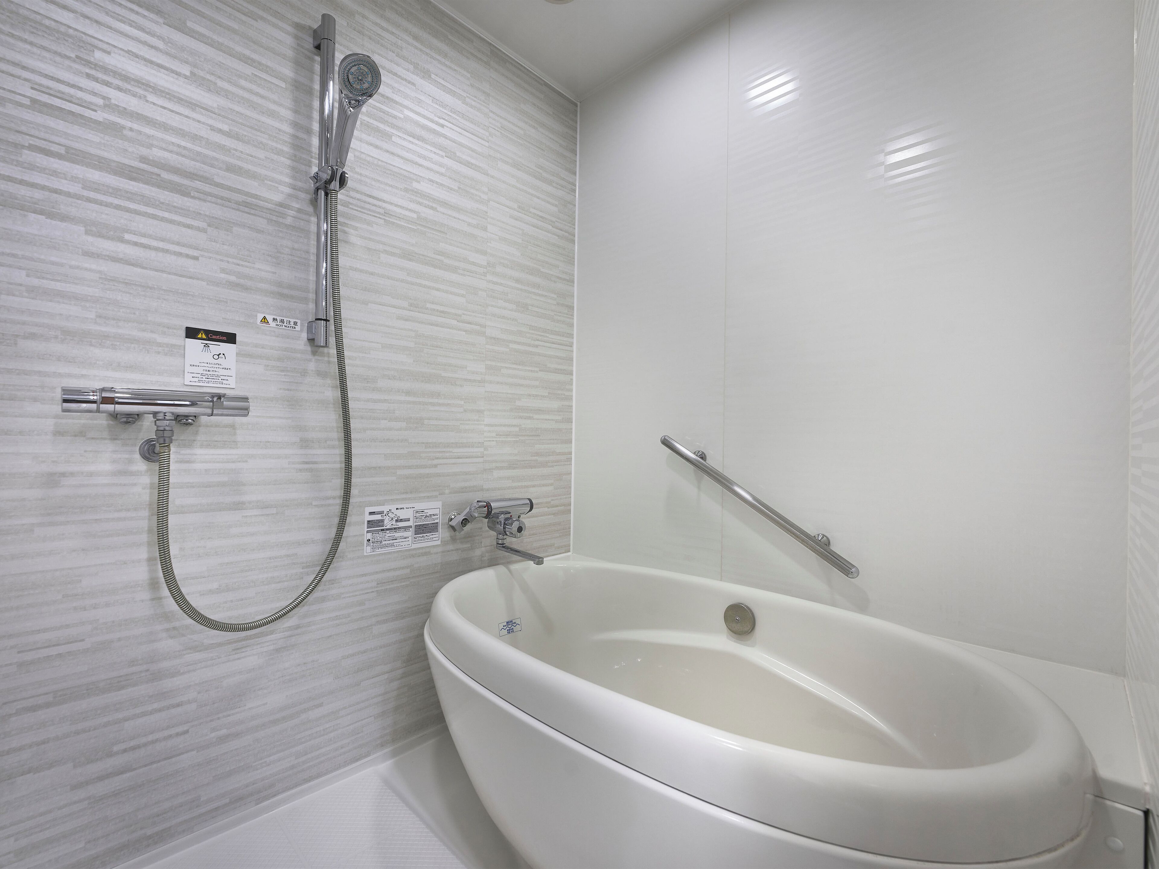 Un baño moderno con una bañera independiente, un cabezal de ducha manual y una barra de apoyo de seguridad.