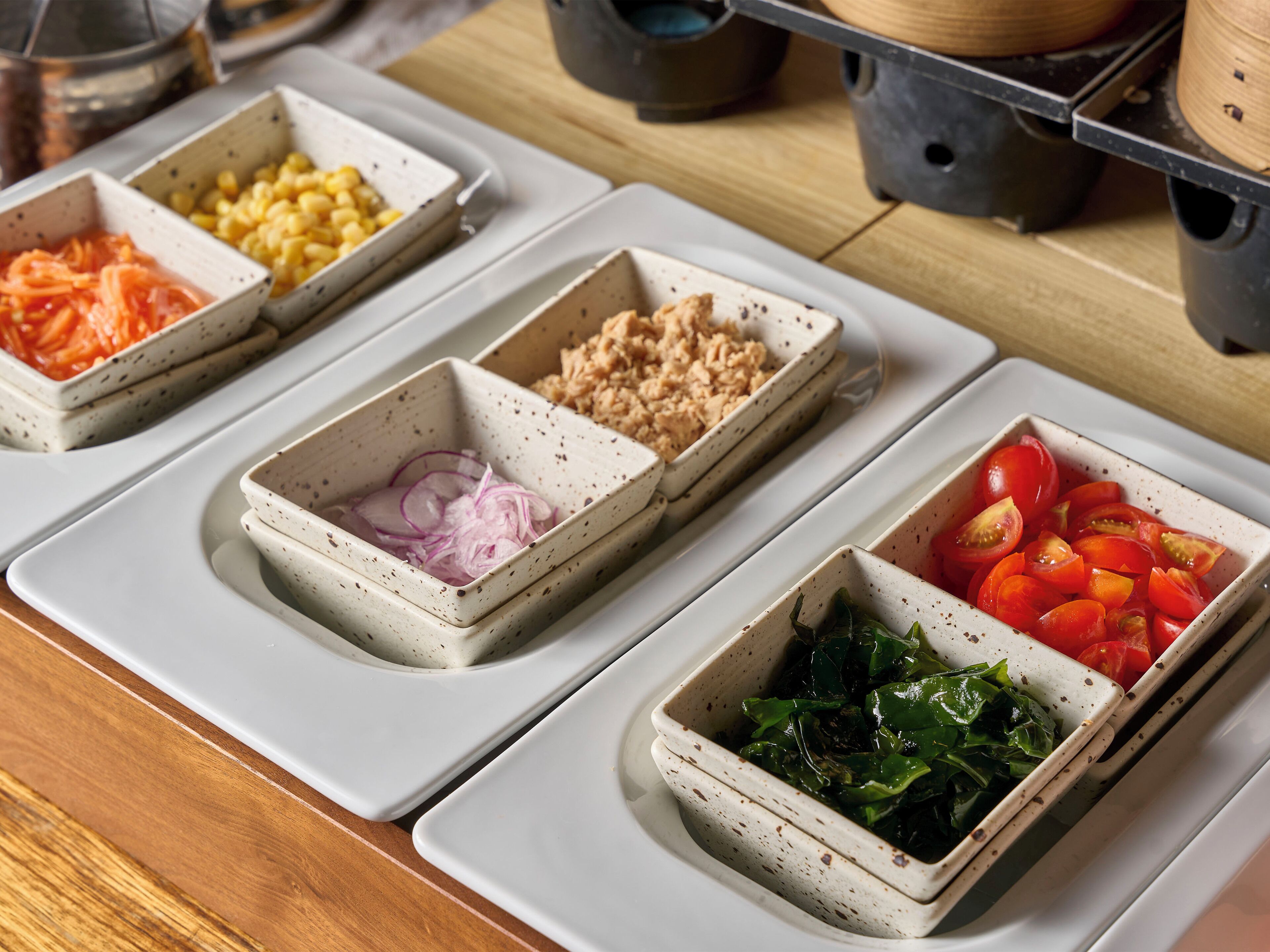 A kitchen counter with four square ceramic dishes containing different food items.