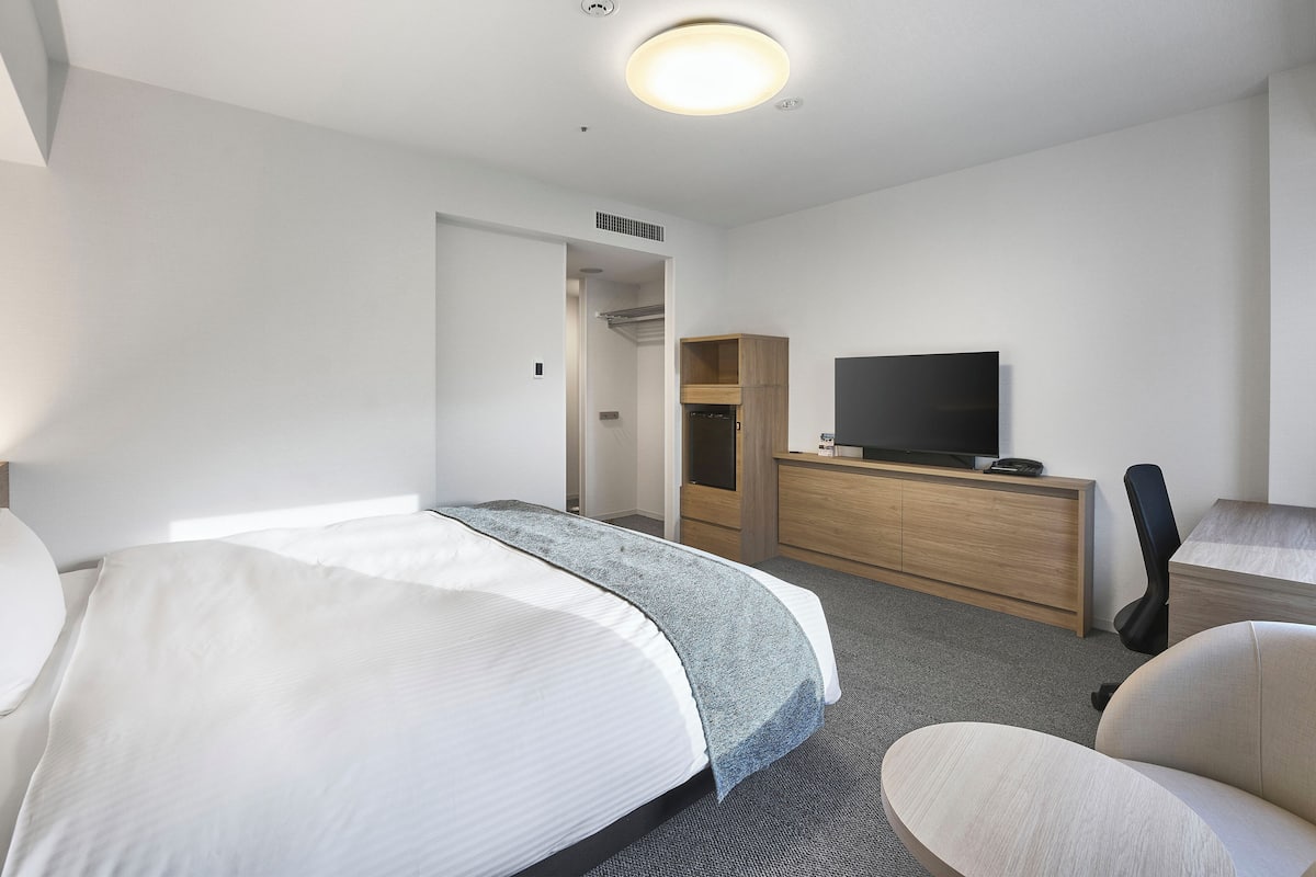 Quarto de hotel com cama, secretária, televisão de tela plana, cadeira e closet espaçoso.