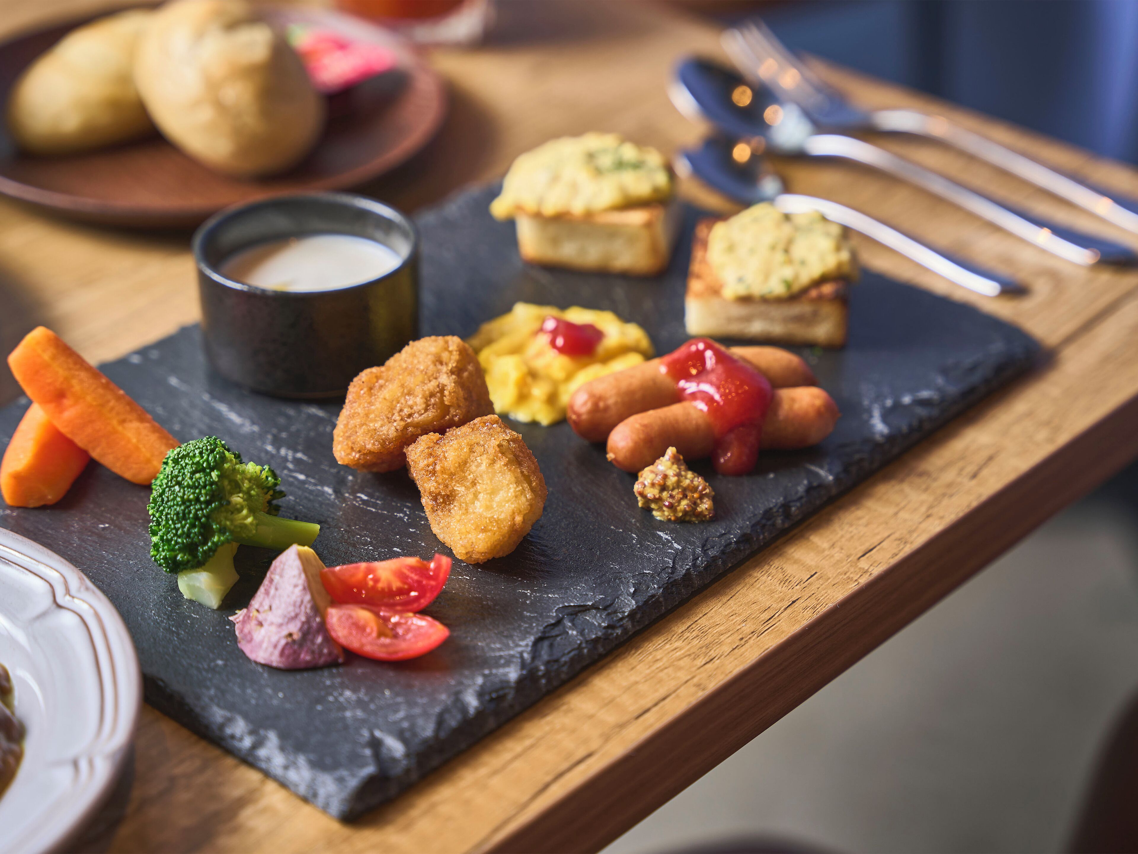 A slate serving board with various finger foods including breaded items, vegetables, and sauces.