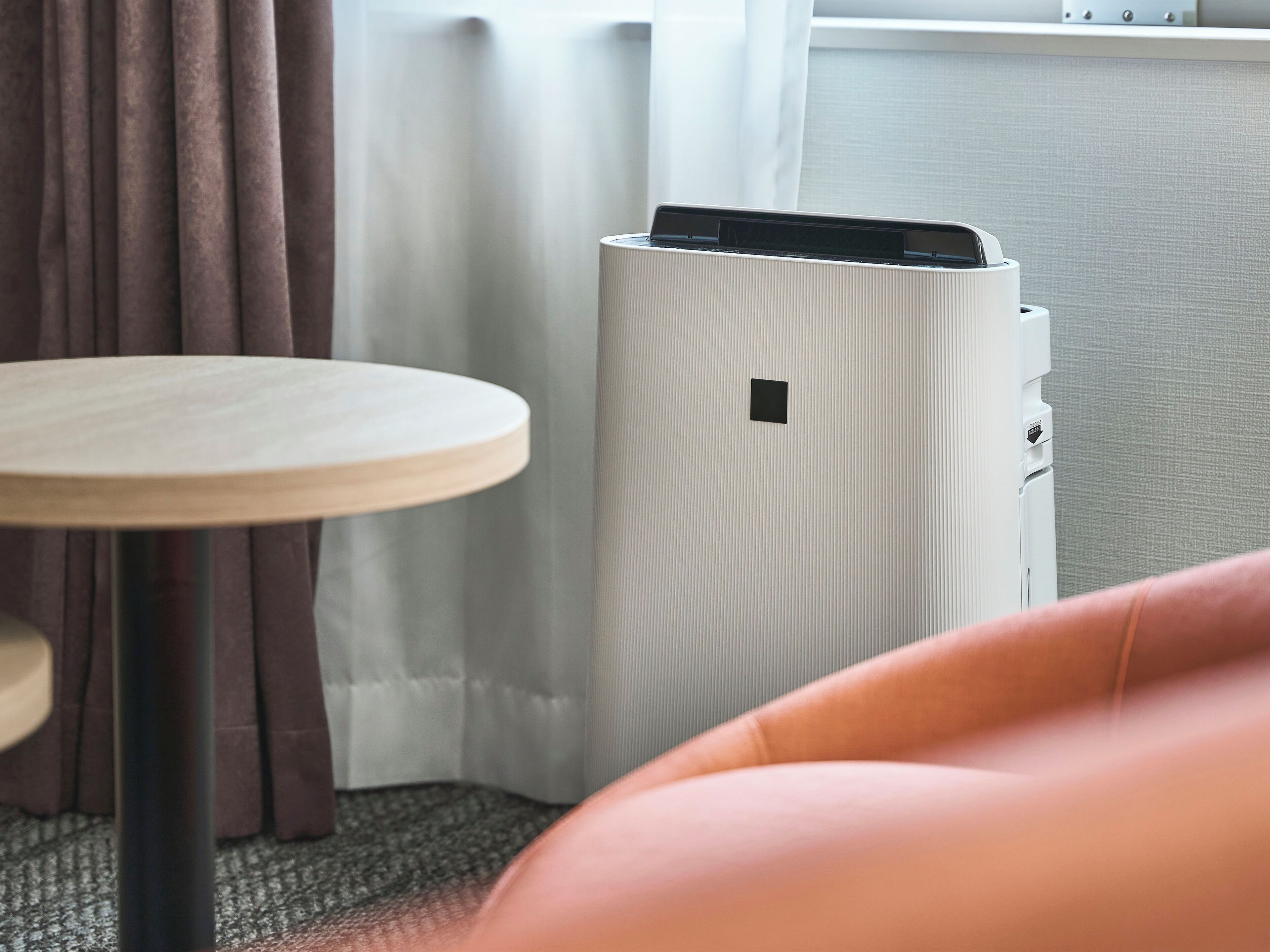 A room with a round wooden table, a white radiator, and a brown curtain.