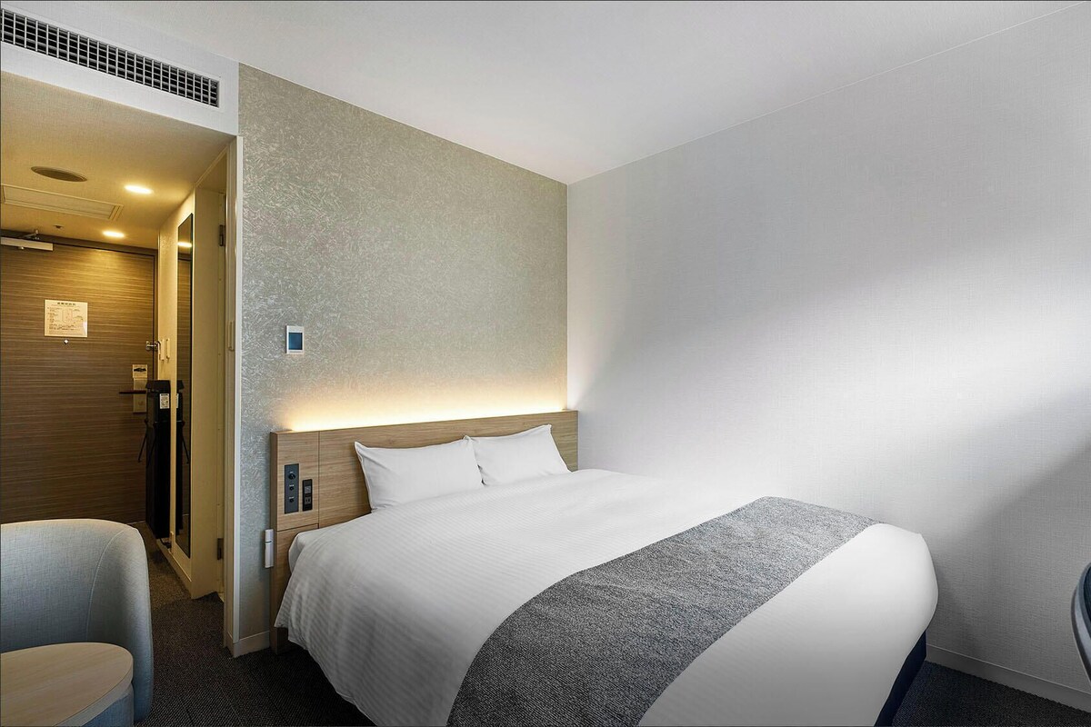 A hotel room with a bed, a desk, a chair, and a shower area.