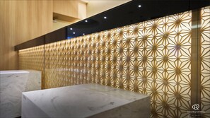 A reception area with a geometric patterned wall, marble reception desk, and a wooden panel backdrop.