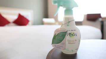 Eine Sprühflasche mit dem Aufdruck 'Fabric & Air Freshener' auf einer Holzoberfläche in einem Hotelzimmer.