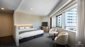 A modern hotel room with a large bed, a desk, two chairs, and a TV.