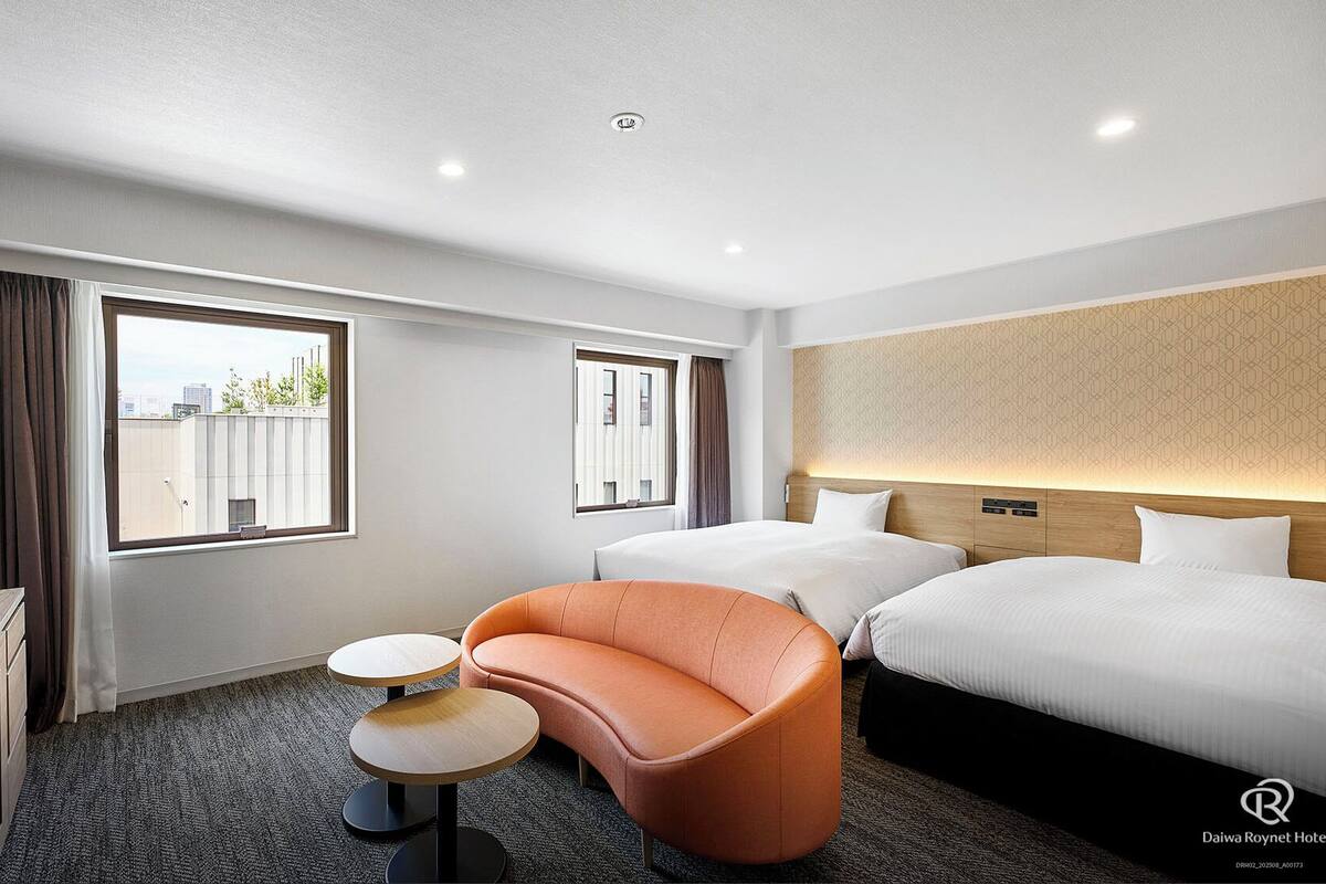 Quarto de hotel com duas camas, um sofá, uma mesa de escritório e duas janelas.