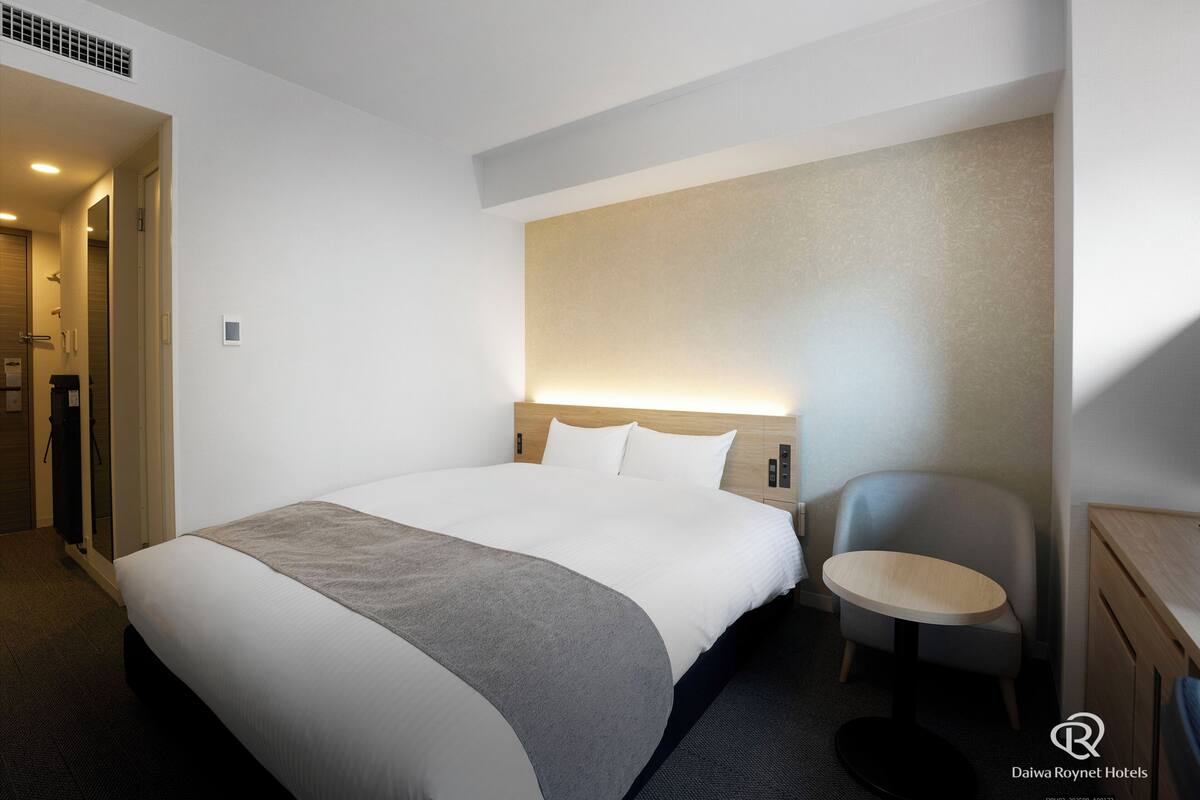 Quarto de hotel com uma cama grande, mesa de cabeceira, uma cadeira e uma pequena escrivaninha.
