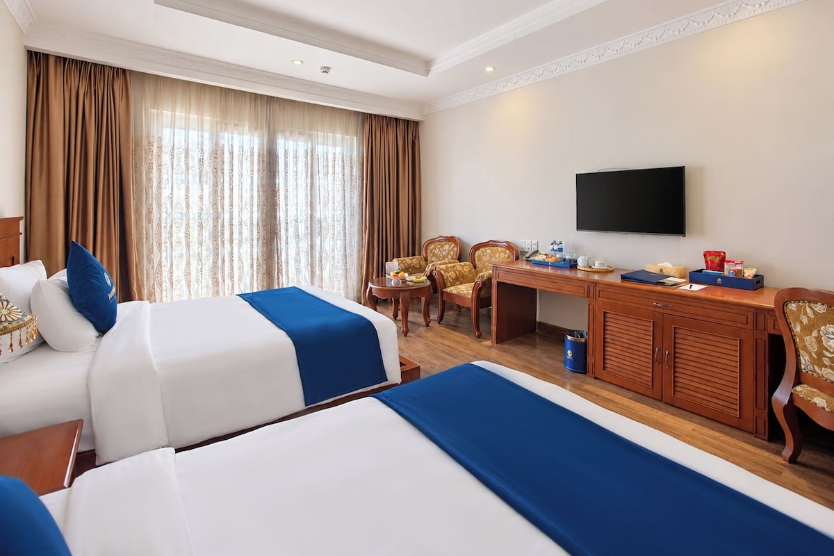 Een hotelkamer met twee bedden, een bureau, een televisie en een eethoek.