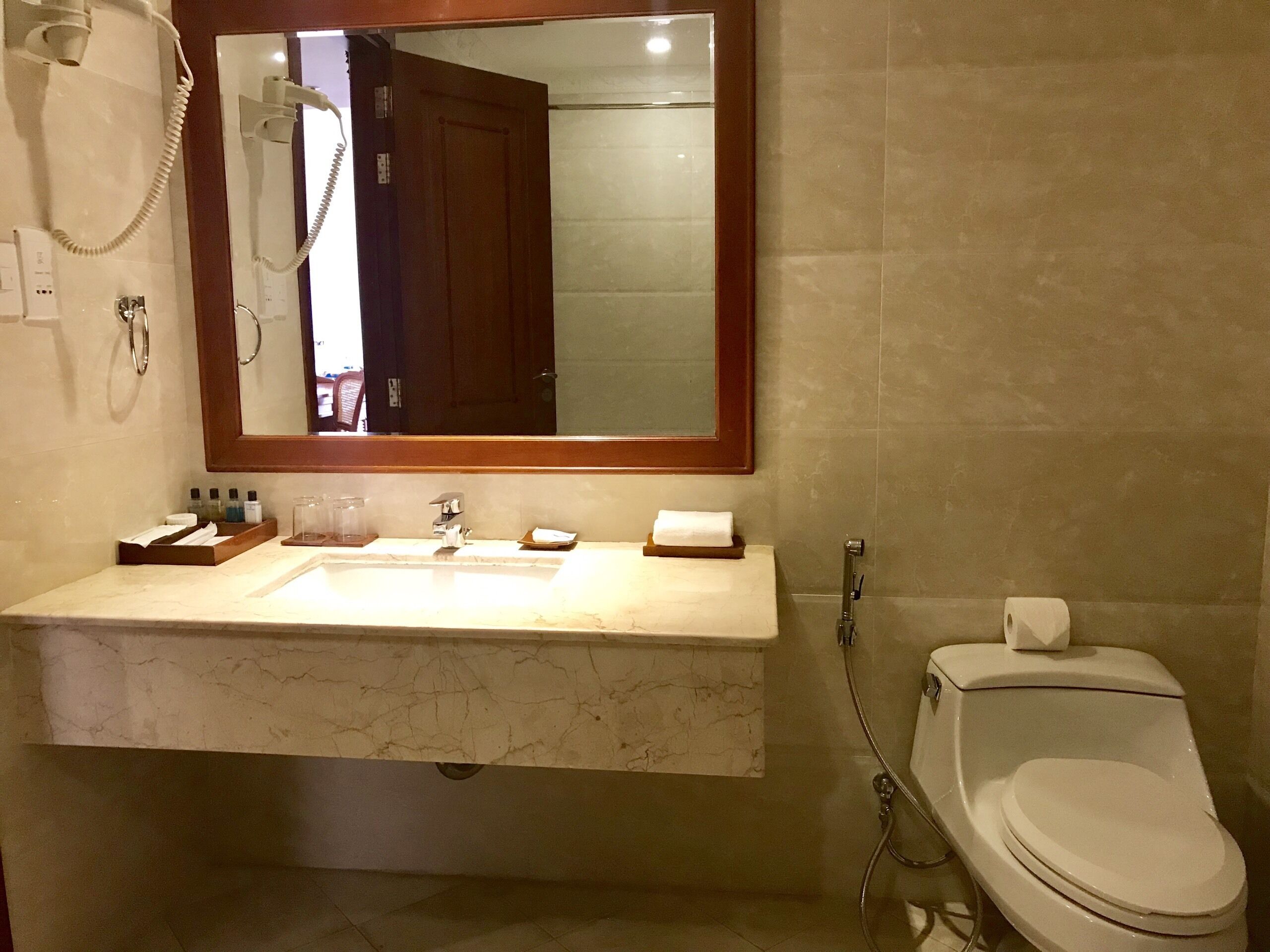 Un baño con lavamanos de mármol, un espejo, inodoro y ducha.