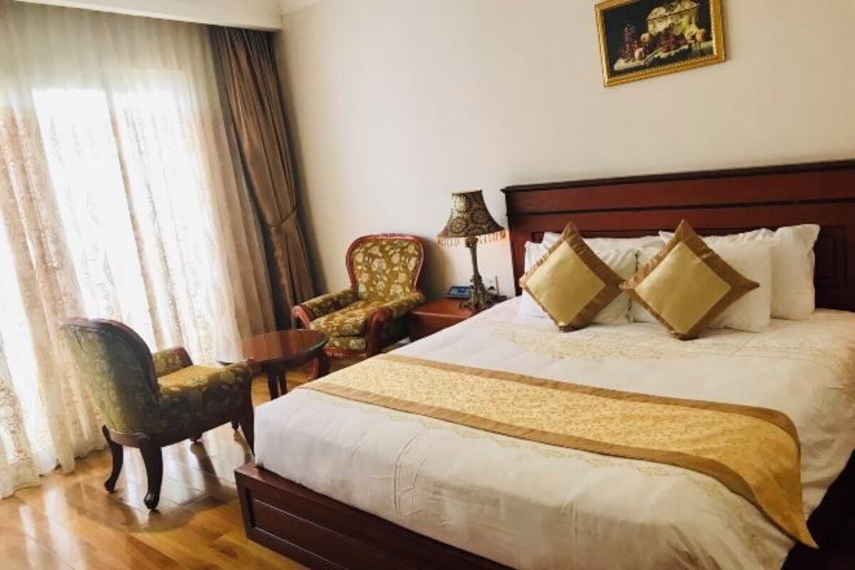 Une chambre d’hôtel avec un grand lit, deux chaises, une table et une lampe.