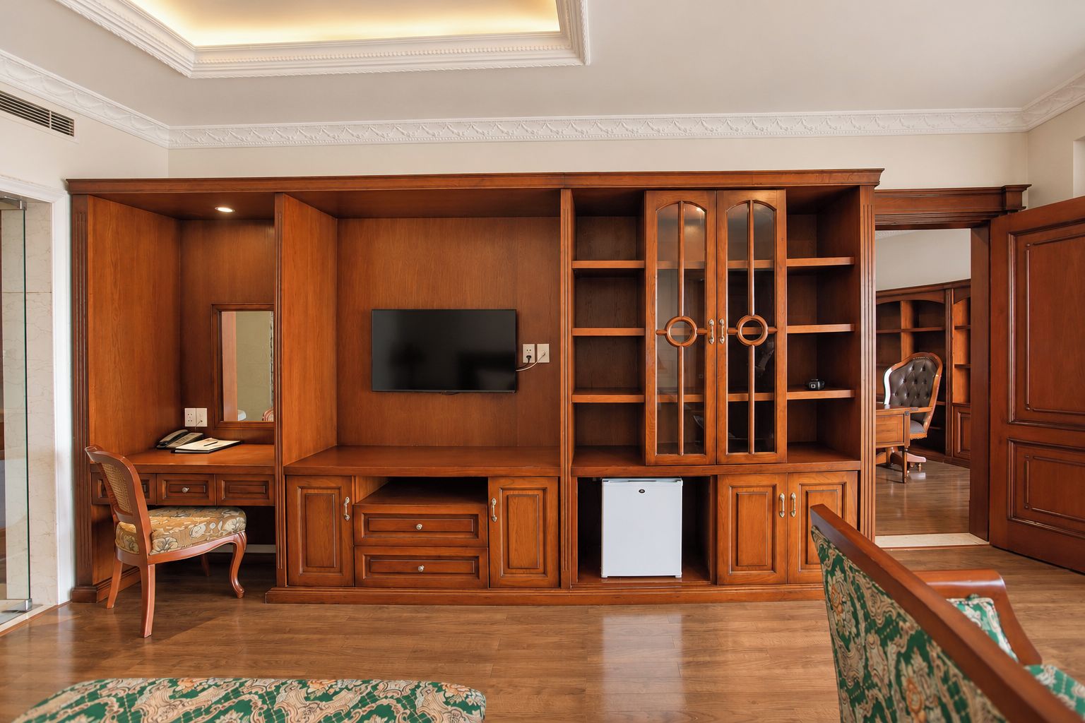 A spacious living room with a built-in entertainment unit, a flat-screen TV, and a small refrigerator.