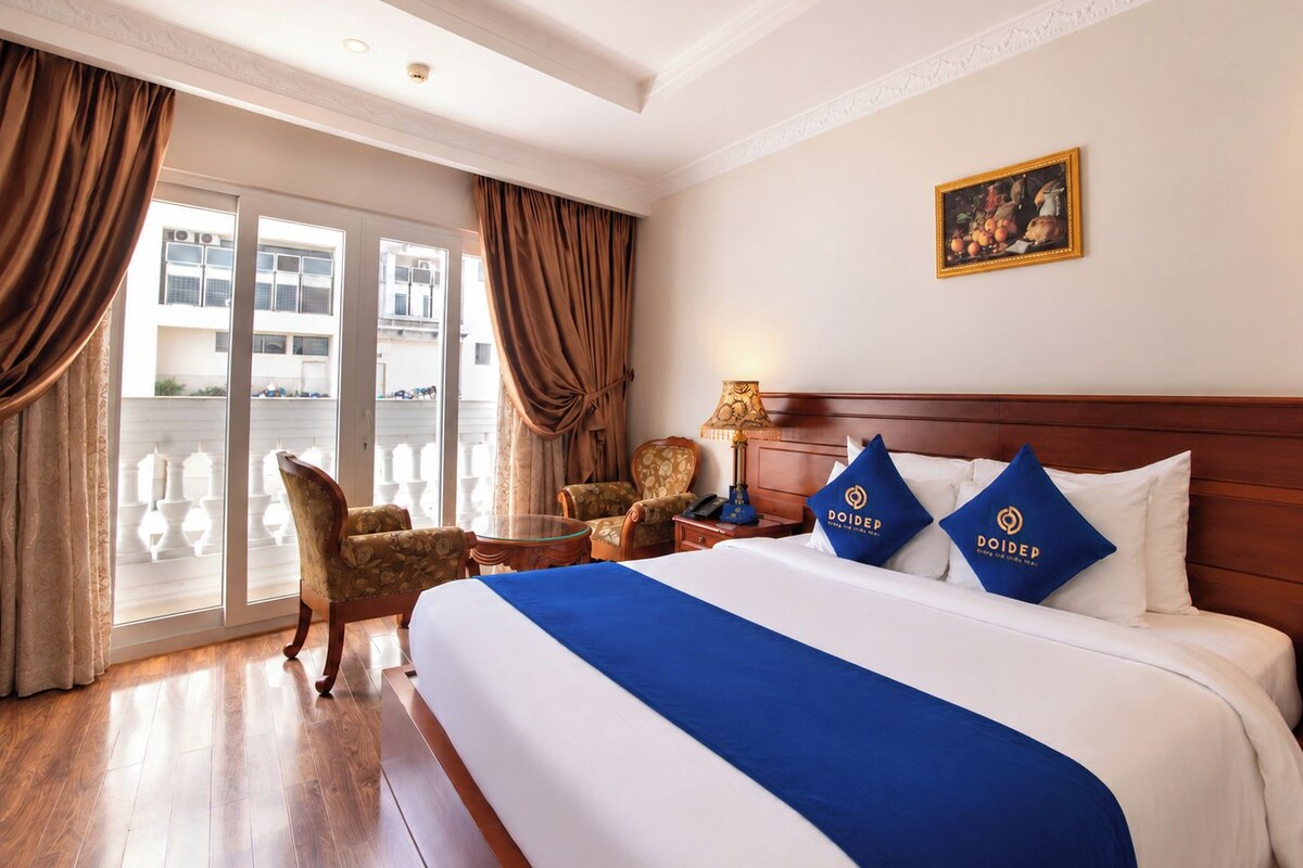 Een hotelkamer met een groot bed, een nachtkastje, een lamp, een stoel en uitzicht op het balkon.