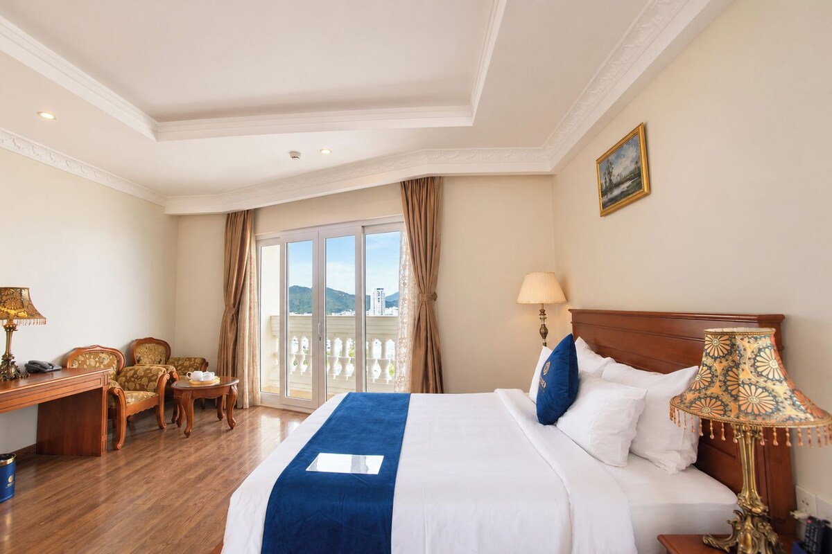 Une chambre d’hôtel avec un grand lit, un bureau, une chaise, une lampe et une vue sur l’extérieur.