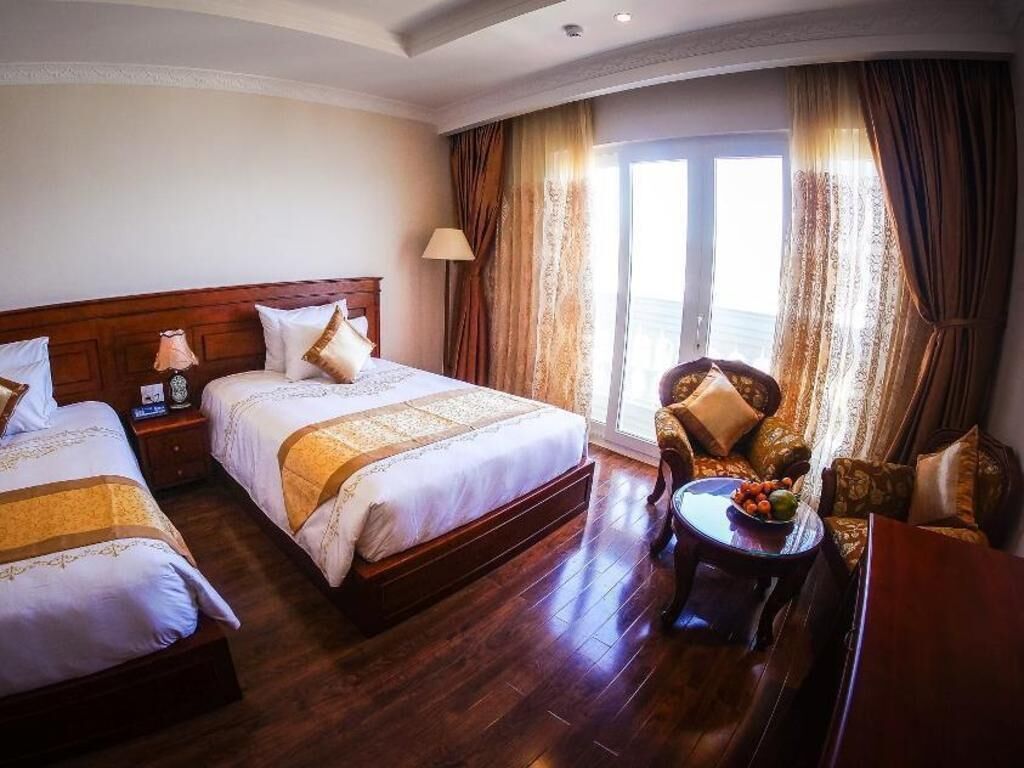 Een hotelkamer met twee bedden, een zithoek met een stoel en tafel, en een groot raam met gordijnen.