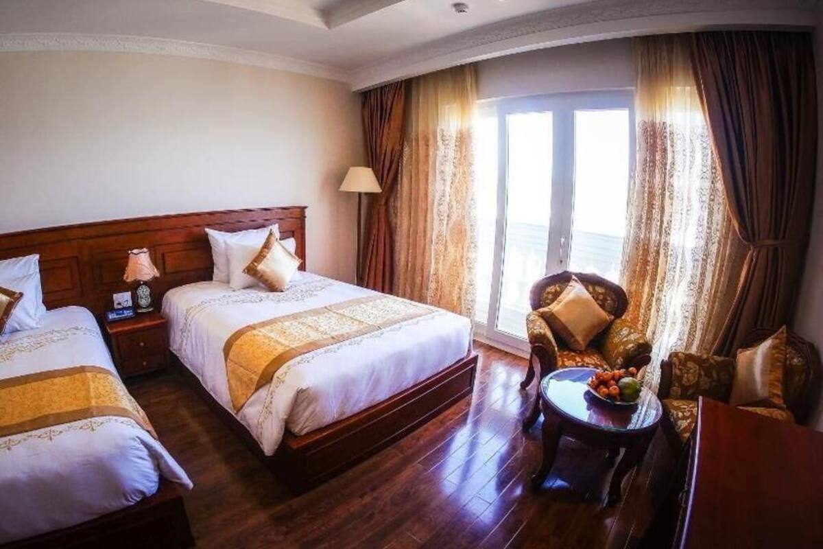 Ein Hotelzimmer mit zwei Betten, einer Sitzecke mit Stuhl und Tisch sowie einem großen Fenster mit Vorhängen.