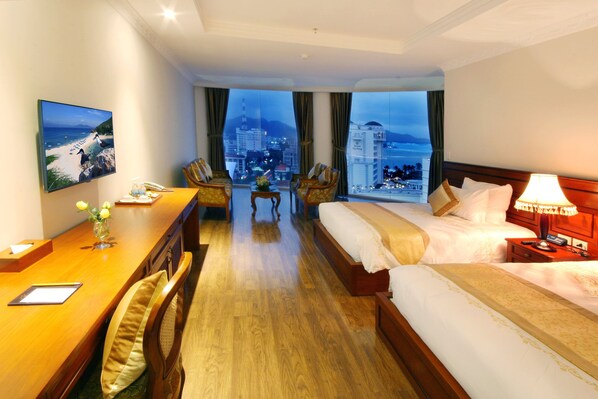 A hotel room with a bed, a desk, a chair, a TV, and a view of the cityscape.
