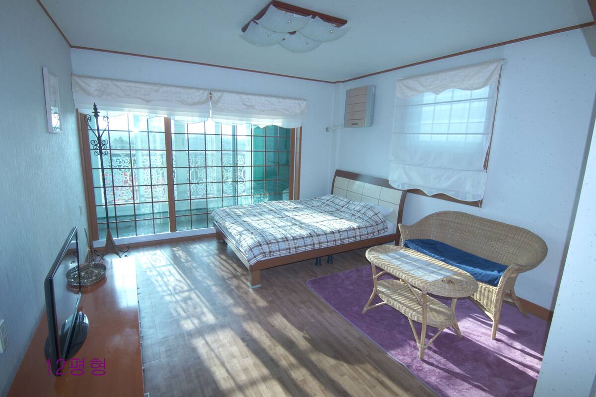 A bedroom with a bed, a chair, a table, a TV, and a window with a view.