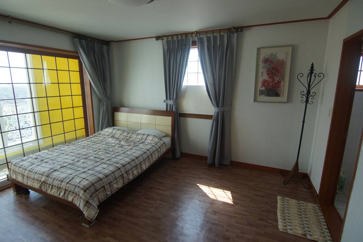 A bedroom with a bed, curtains, a window, and a floor lamp.