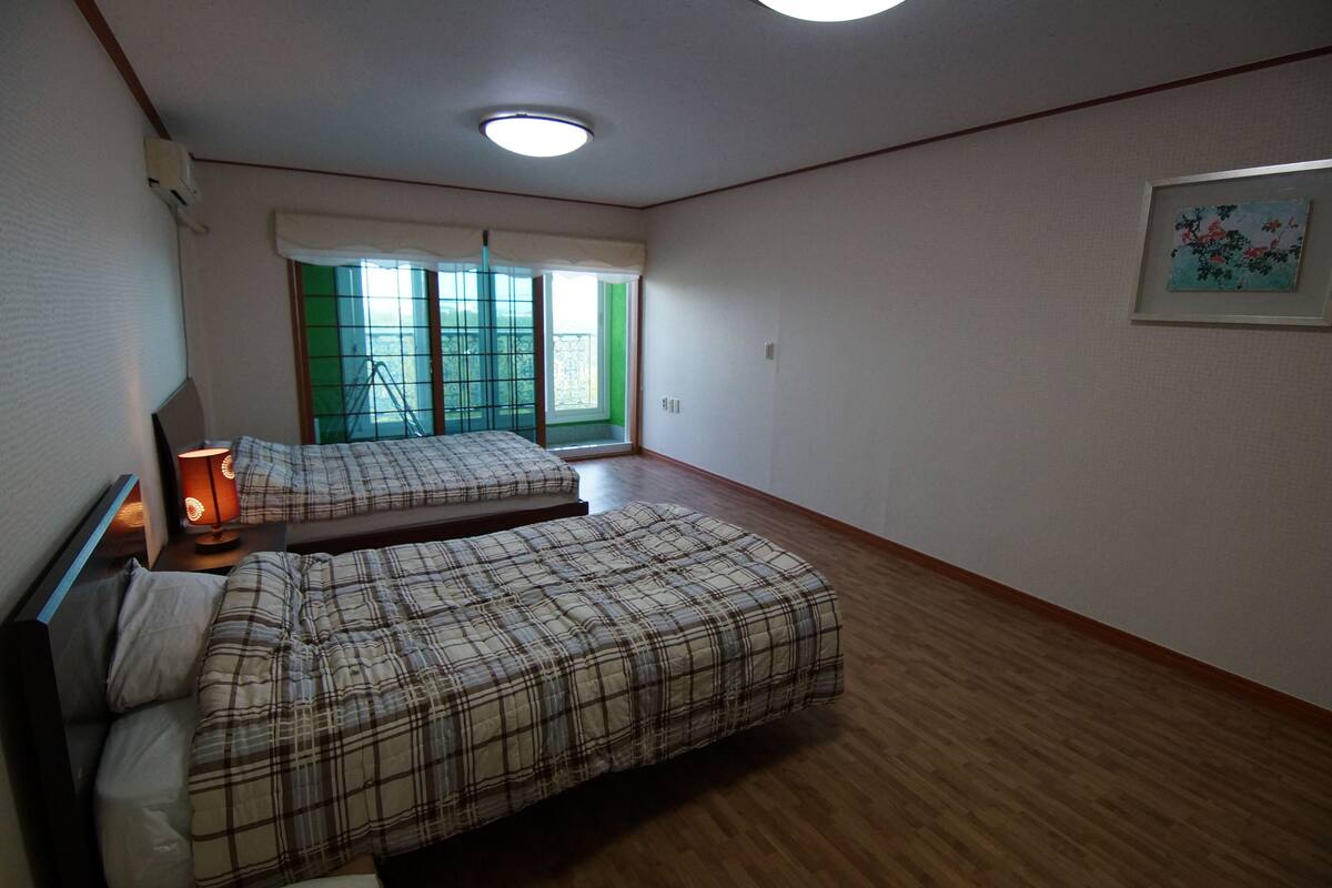 A bedroom with two beds, a window with a view, and a ceiling light.