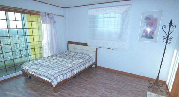 Un dormitorio con cama, ventana con cortinas, un cuadro en la pared y una lámpara de pie.