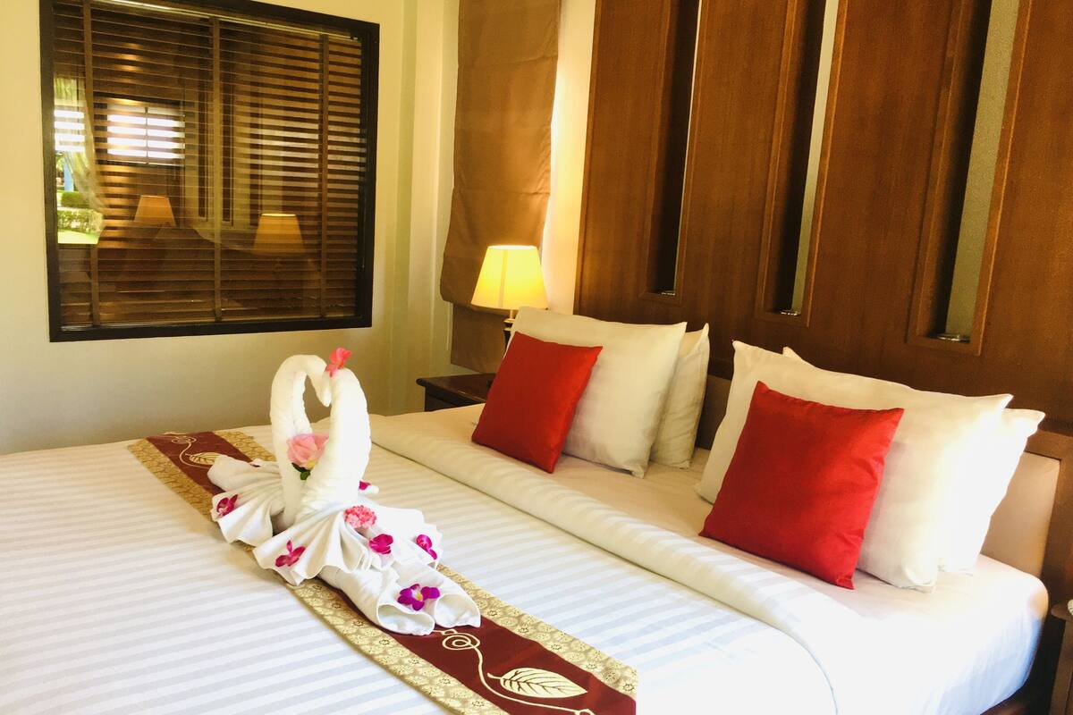 A hotel room with a neatly made bed, a window with blinds, a bedside lamp, and a wooden door.