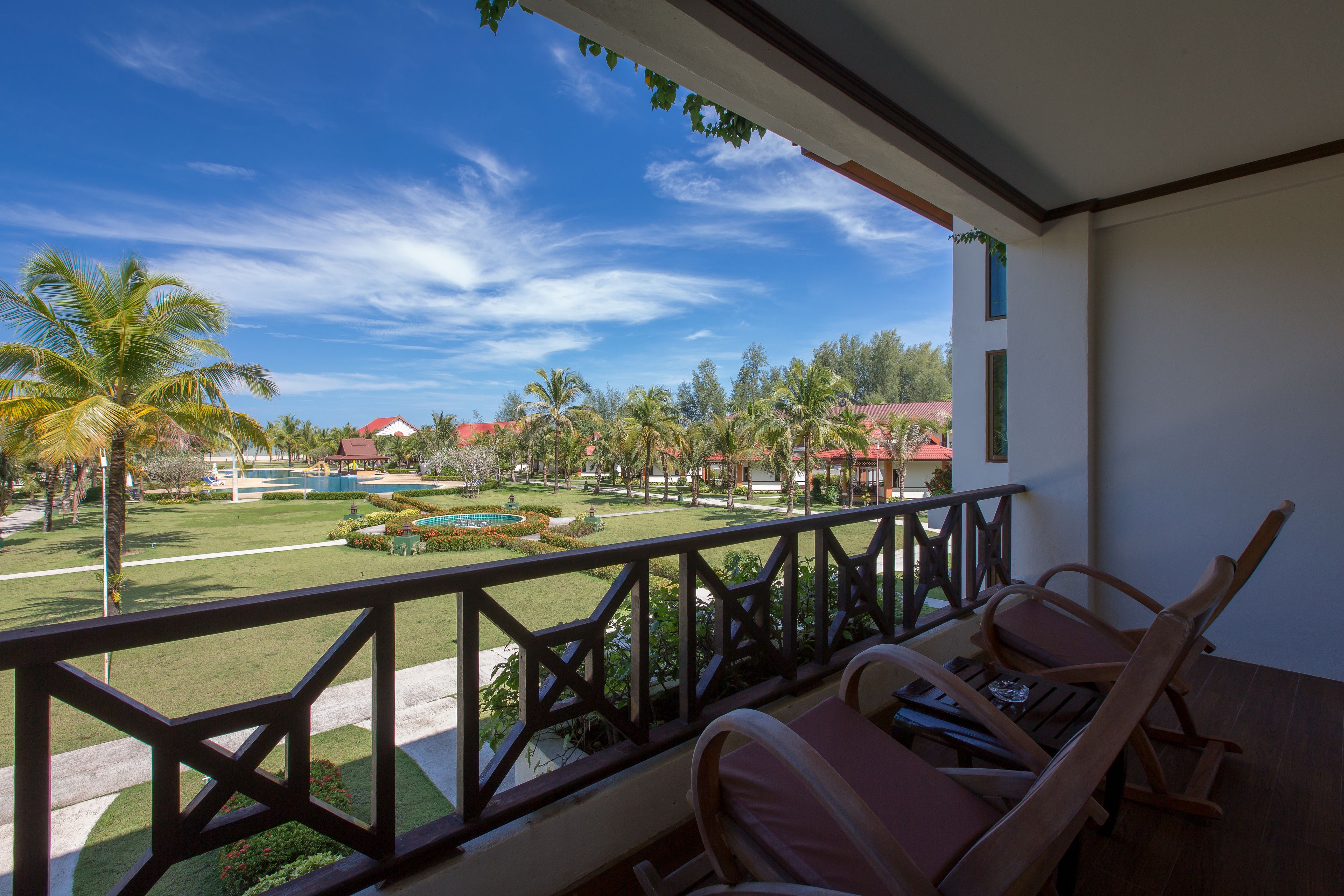 A balcony with a view of a landscaped garden, palm trees, and a pool.