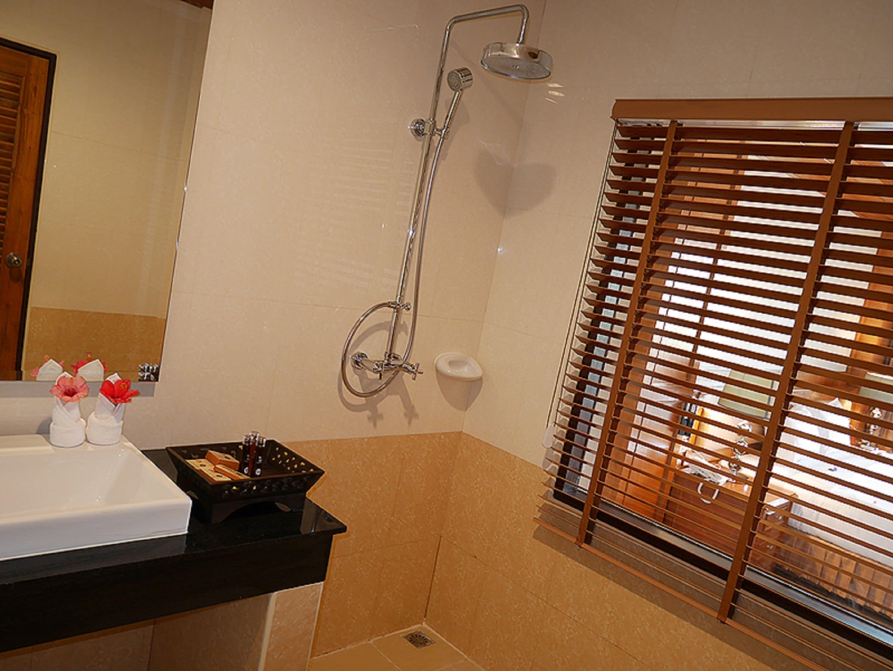 A bathroom with a shower, a sink, and a window with blinds.