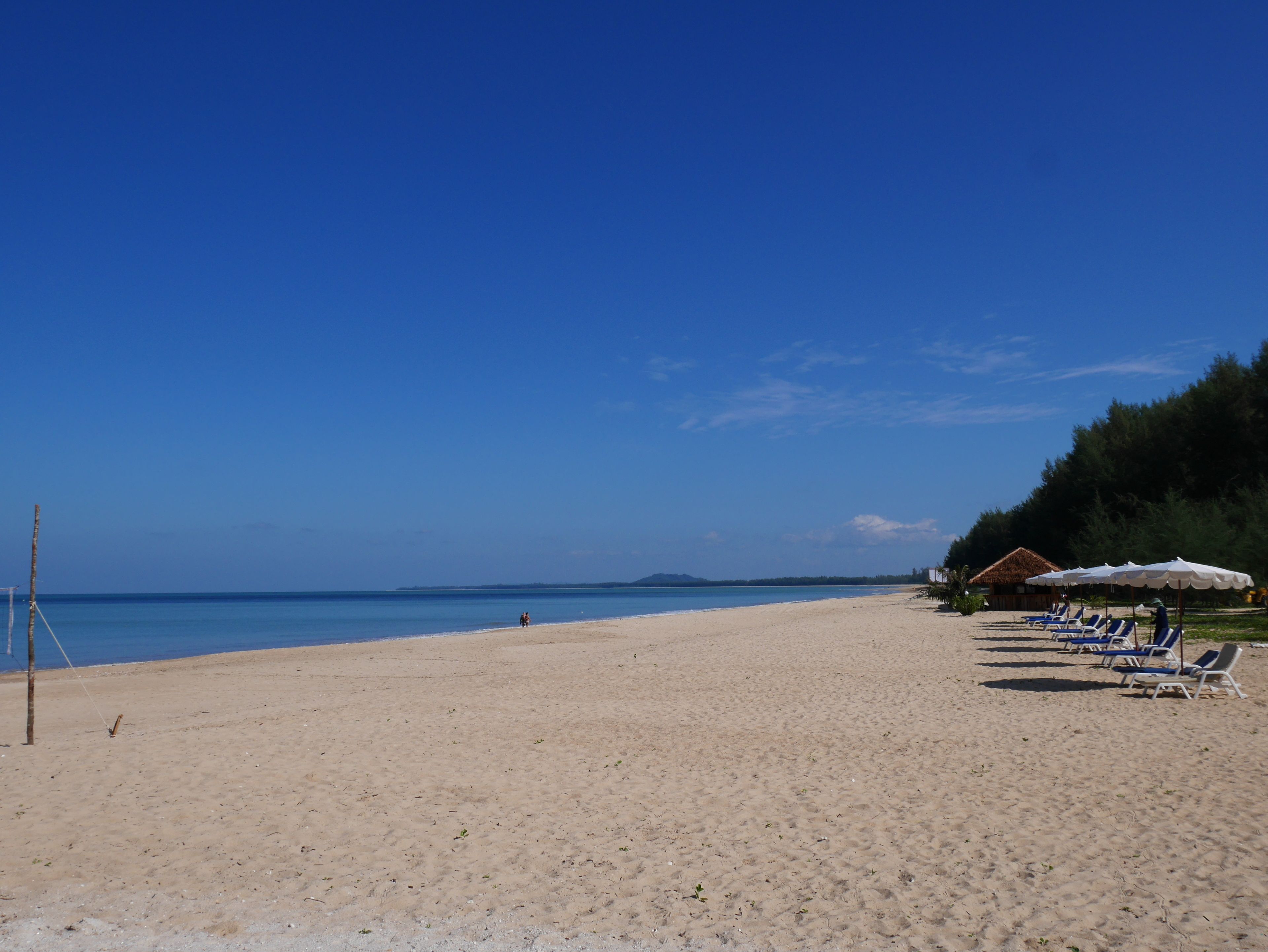 A beach with clear skies, a sandy shore, and a few beach chairs and umbrellas.