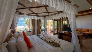A bedroom with a bed, curtains, a TV, and a view of the beach.