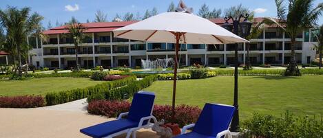 A hotel with a pool area featuring two blue lounge chairs and a large umbrella.