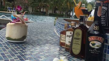 A poolside area with a tiled floor, a drink with a straw, and bottles of Bailey's and other spirits.