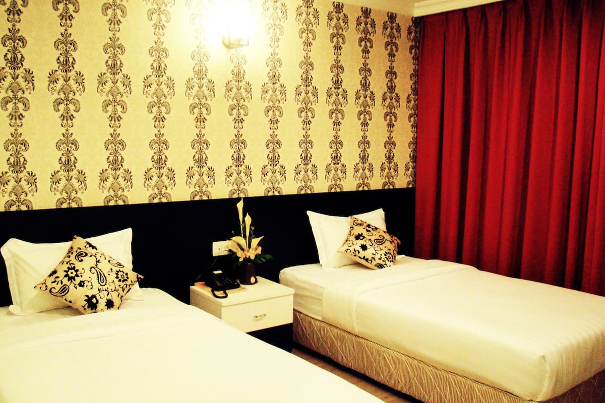 A hotel room with two beds, a nightstand with a phone, and a wall with patterned wallpaper.