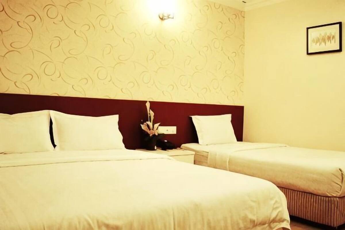 A hotel room with two beds, a nightstand, a wall-mounted light, and a framed picture.