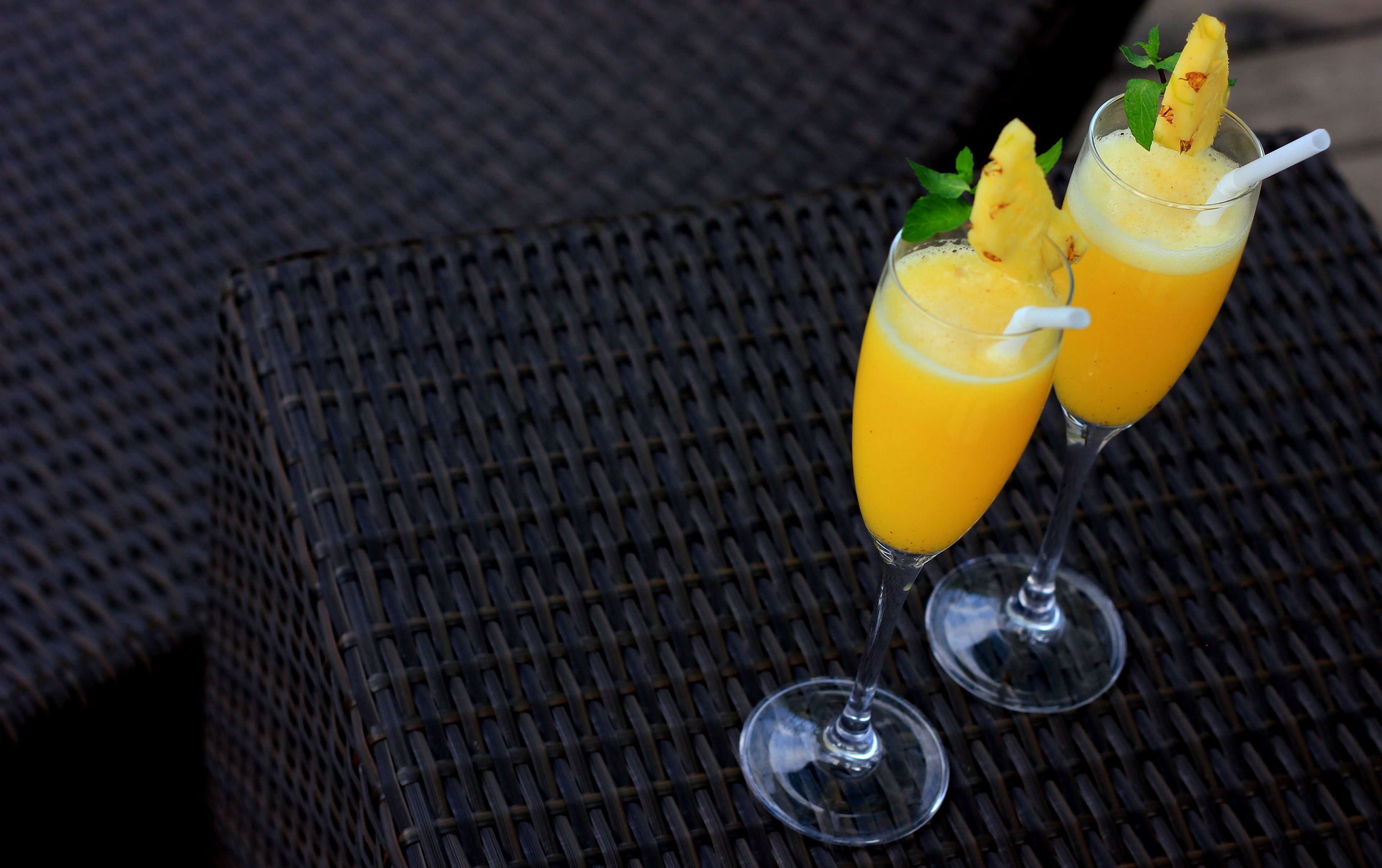 Two glasses of orange juice with pineapple garnish on a woven table.
