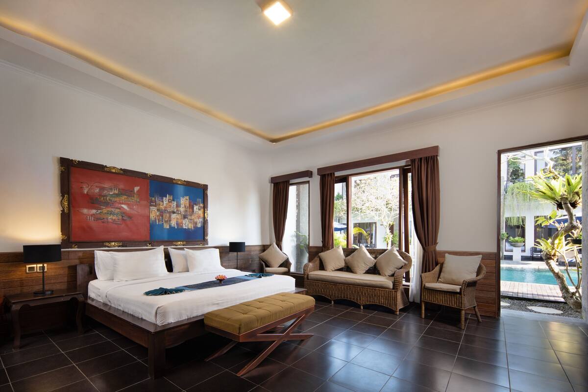 Un dormitorio amplio con una cama grande, un sofá, una silla y vista a una piscina.