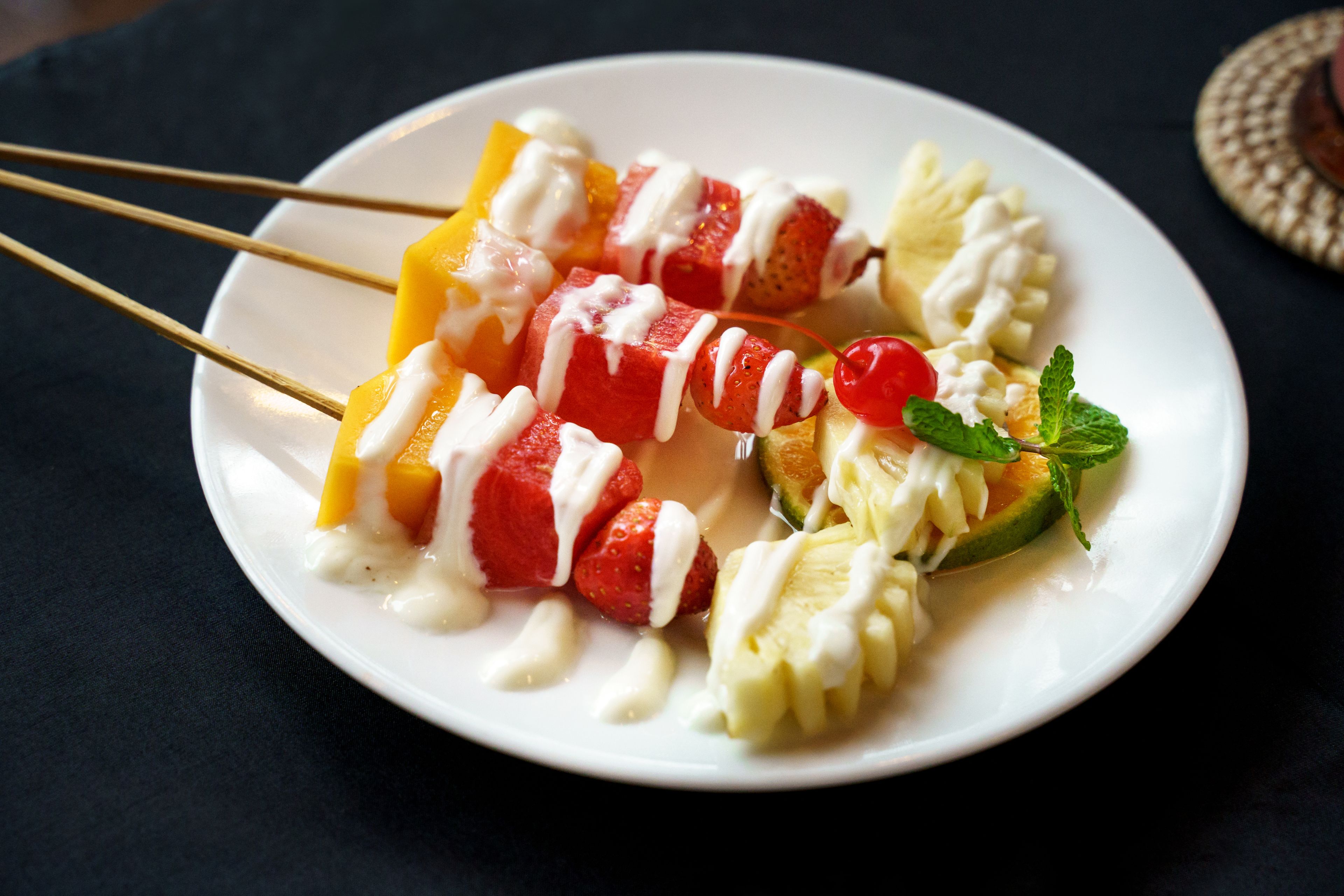 A plate of fruit skewers with white sauce and mint garnish.