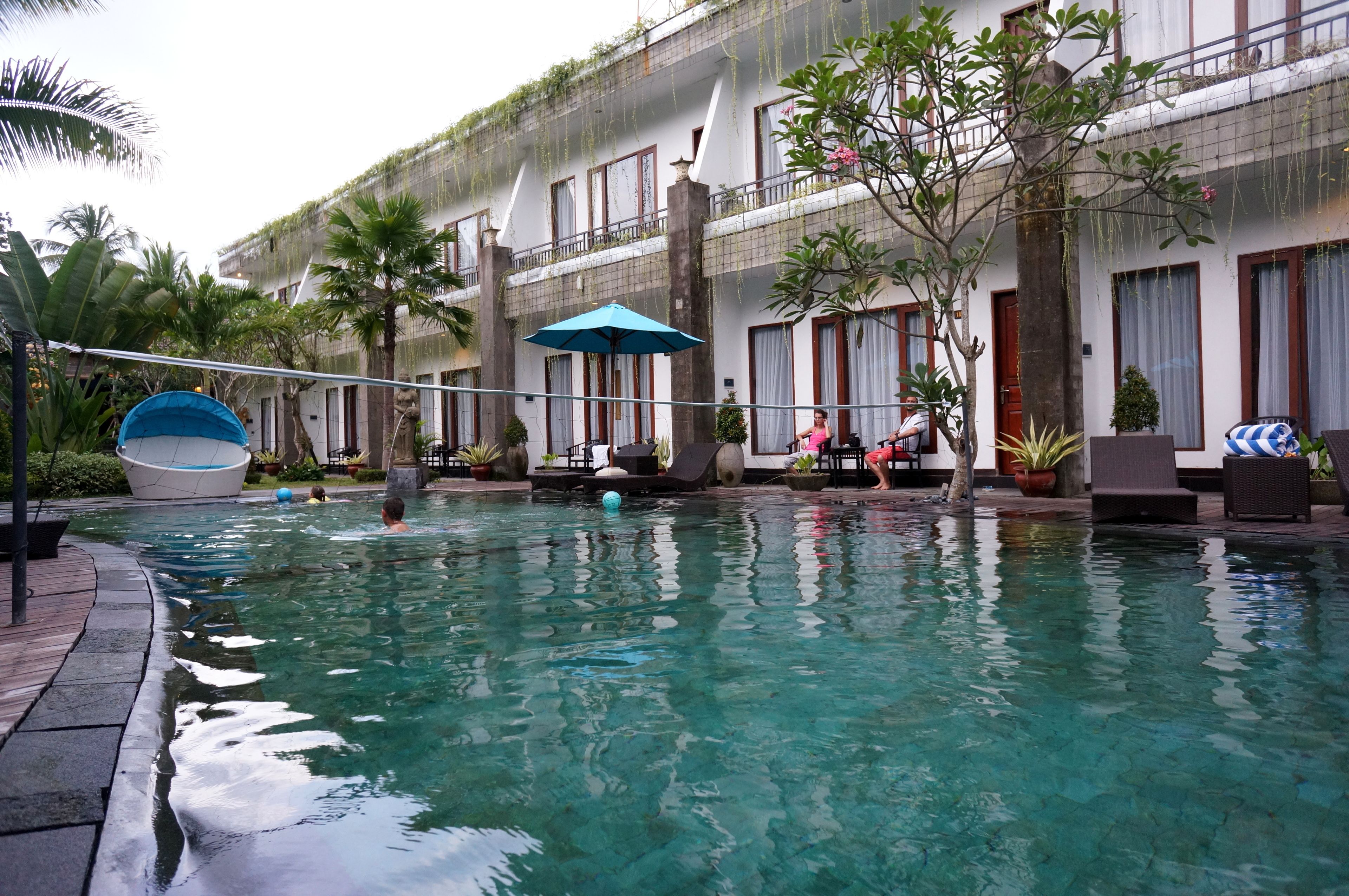 A swimming pool with lounge chairs and umbrellas, surrounded by potted plants and a building with balconies.