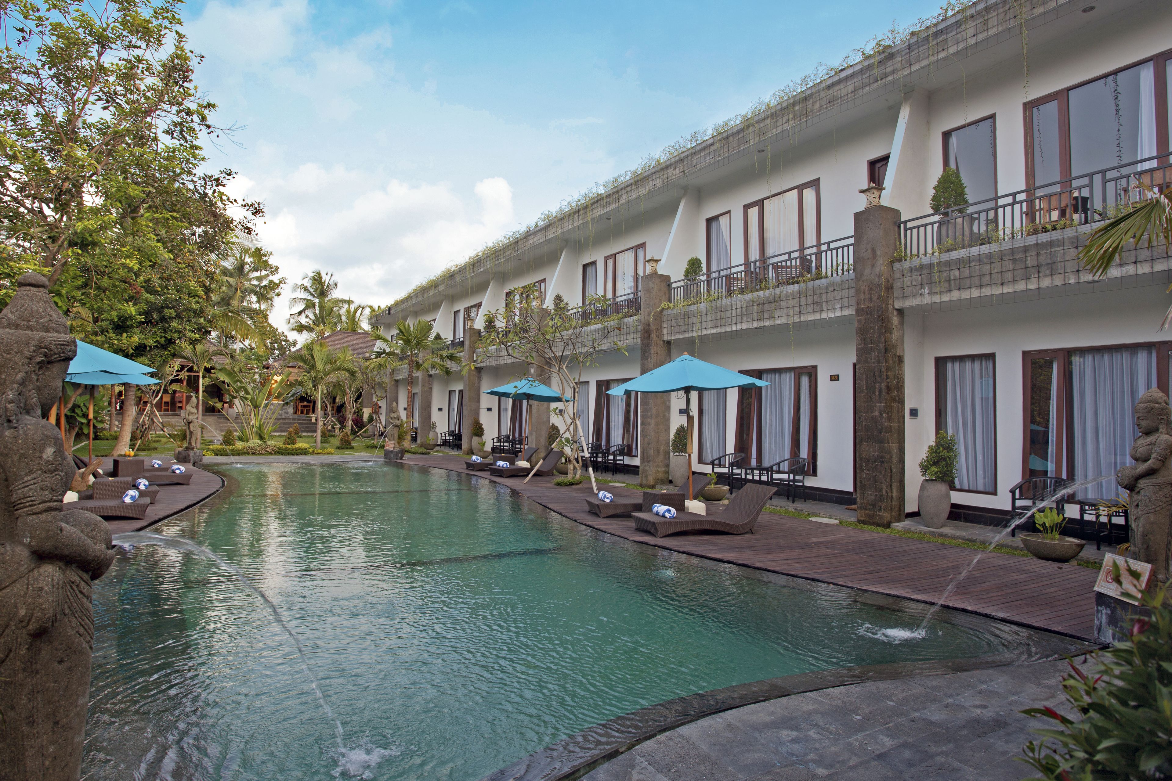 Un hotel con piscina, sillas de descanso y sombrillas.